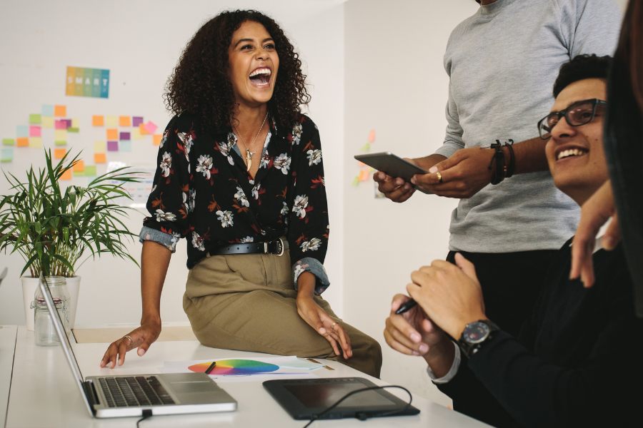 Woman sat on a desk laughing with her co-worker