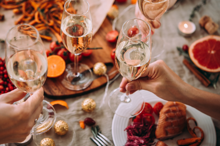 Three people cheers-ing their prosecco glasses over a table set with christmas dinner